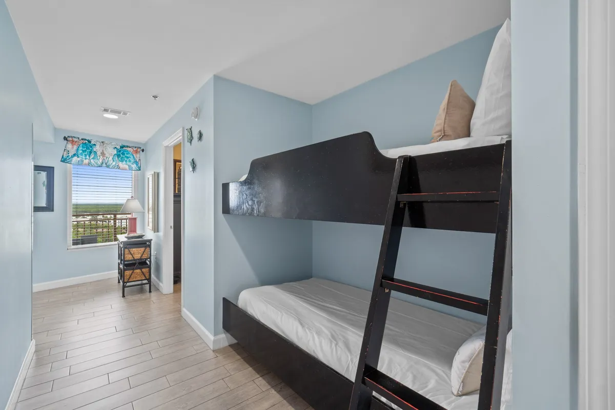 A cozy bunk bed nook with floral curtains framing the window, a nightstand with a lamp, and playful decor. The atmosphere is warm and inviting, ideal for younger travelers to enjoy playful evenings and restful sleep.