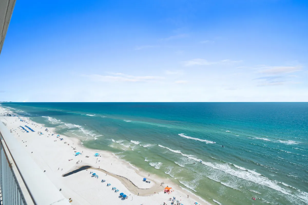 A wide, serene beach scene with golden sand, gentle ocean waves, and an expansive sky. Guests are sunbathing, strolling, and building sandcastles, capturing the essence of a cost-effective beach getaway without compromising on location.