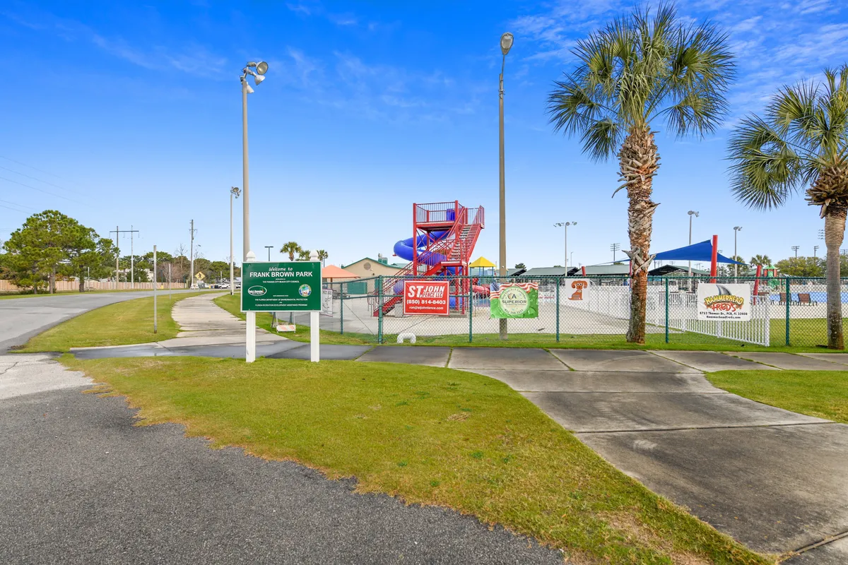 An exterior view of a local water park, showcasing colorful water slides, playground equipment, and tropical palm trees under a sunny sky. Families and children are enjoying various activities, suggesting a range of complimentary or seasonal attractions nearby.