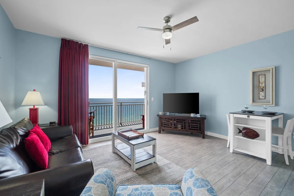 A comfortable living area with large windows showcasing an ocean view, cozy seating, a decorative lamp, and a TV unit. The space is arranged for both relaxation and entertainment, with ample room for unfolding the sleeper sofa for extra guests.