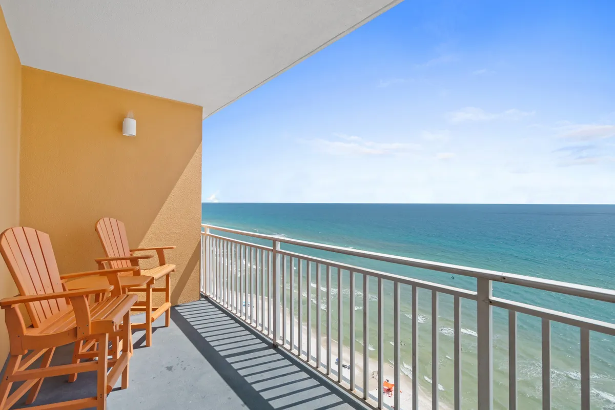 A private balcony with two orange Adirondack chairs overlooks the endless blue of the Gulf, with the ocean horizon and clear sky creating a peaceful, secluded atmosphere. The sun casts gentle shadows from the railing onto the floor, suggesting an inviting spot for morning coffee or sunset drinks.