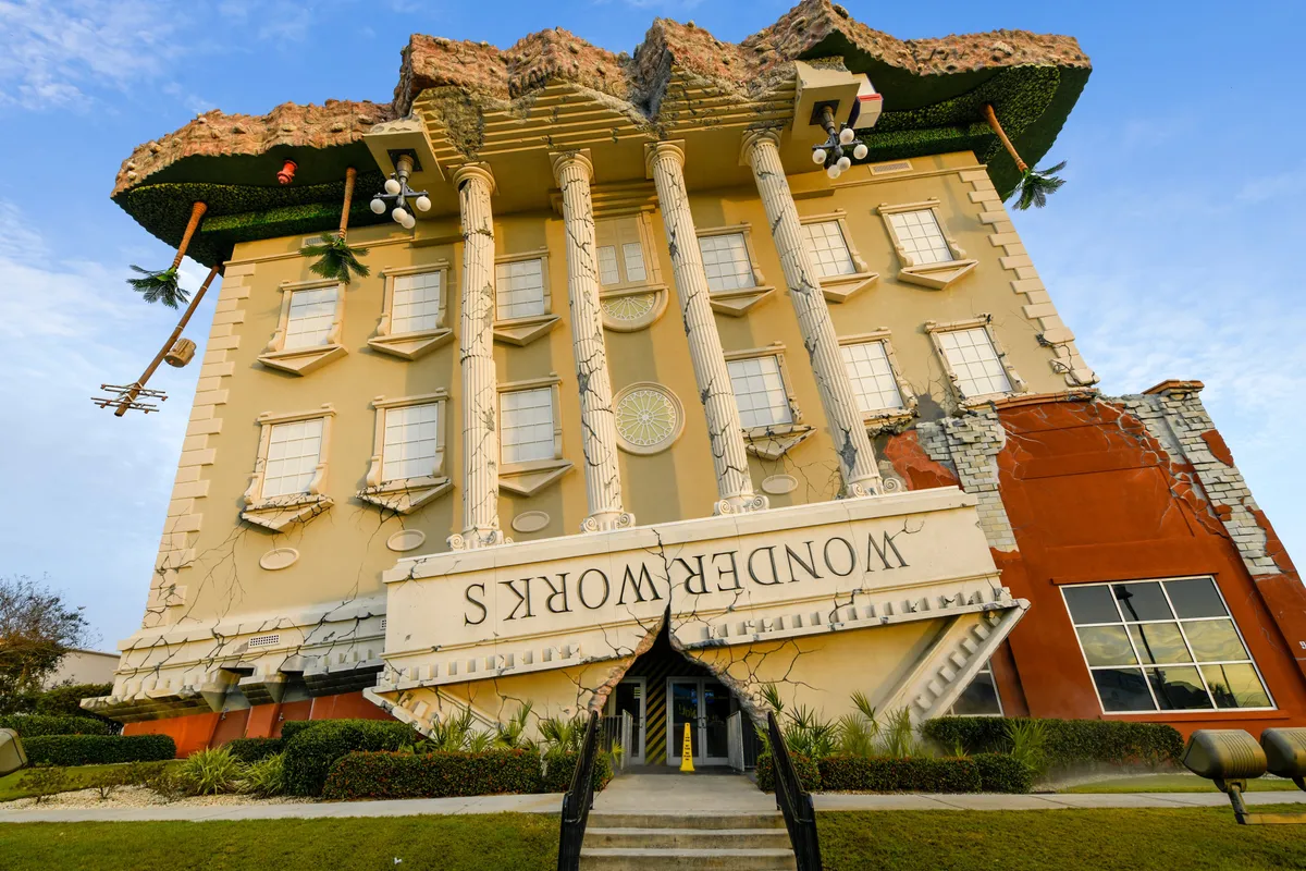 The whimsical upside-down WonderWorks building, with its large columns and creative architecture, stands out as a playful local attraction. The entrance pathway invites visitors to explore this interactive science and amusement attraction, perfect for families and groups.